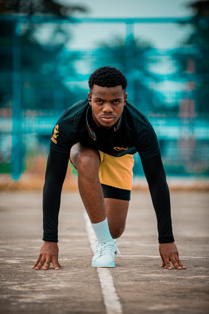 A young male athlete in action while preparing to sprint on an outdoor track.